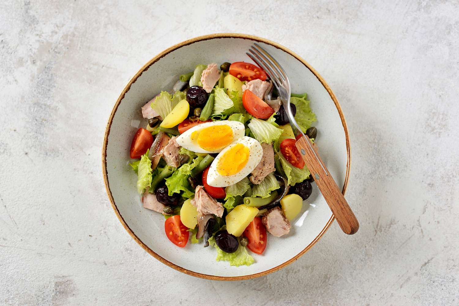 French salad Nicoise with tuna, boiled potatoes, egg, green beans, tomatoes, dried olives, lettuce and anchovies. Top View.