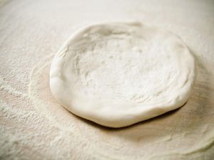 Close up of pizza dough being flattened.