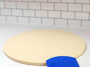 Cast Elegance Round Pizza Stone and plastic scraper on a kitchen counter