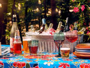 An outdoor table with a selection of wines, glasses, and cups