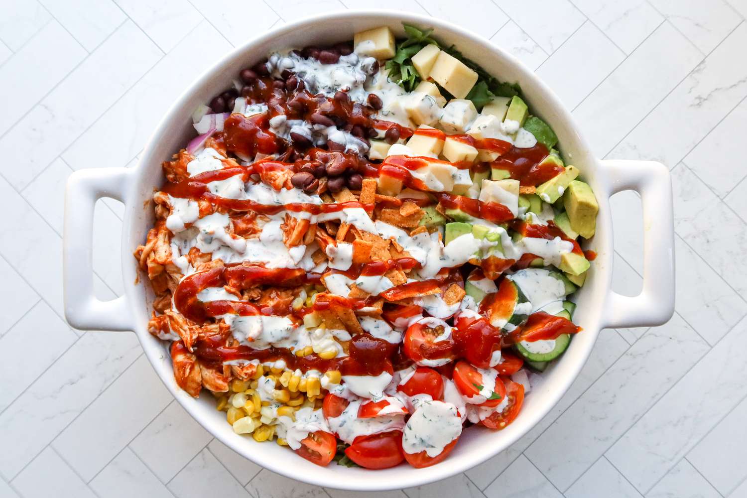 A white baking dish with a colorful bbq ranch chicken salad with white and red sauces on top