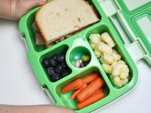 Child's hand touching Bentgo Kids' Lunch Box containing food