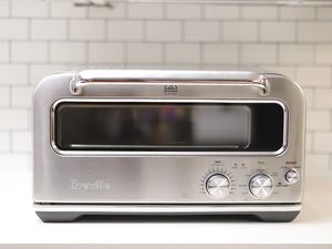 Breville The Smart Oven Pizzaiolo displayed on white countertop with white tile backsplash in background