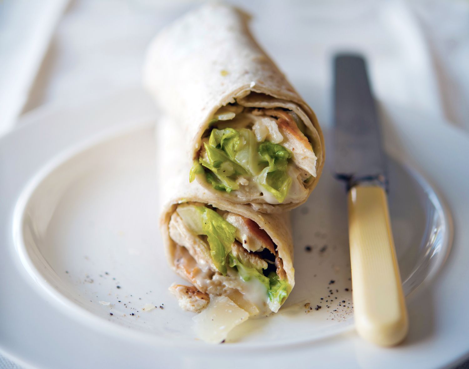 A chicken Caesar wrap cut in half and resting on a white plate 