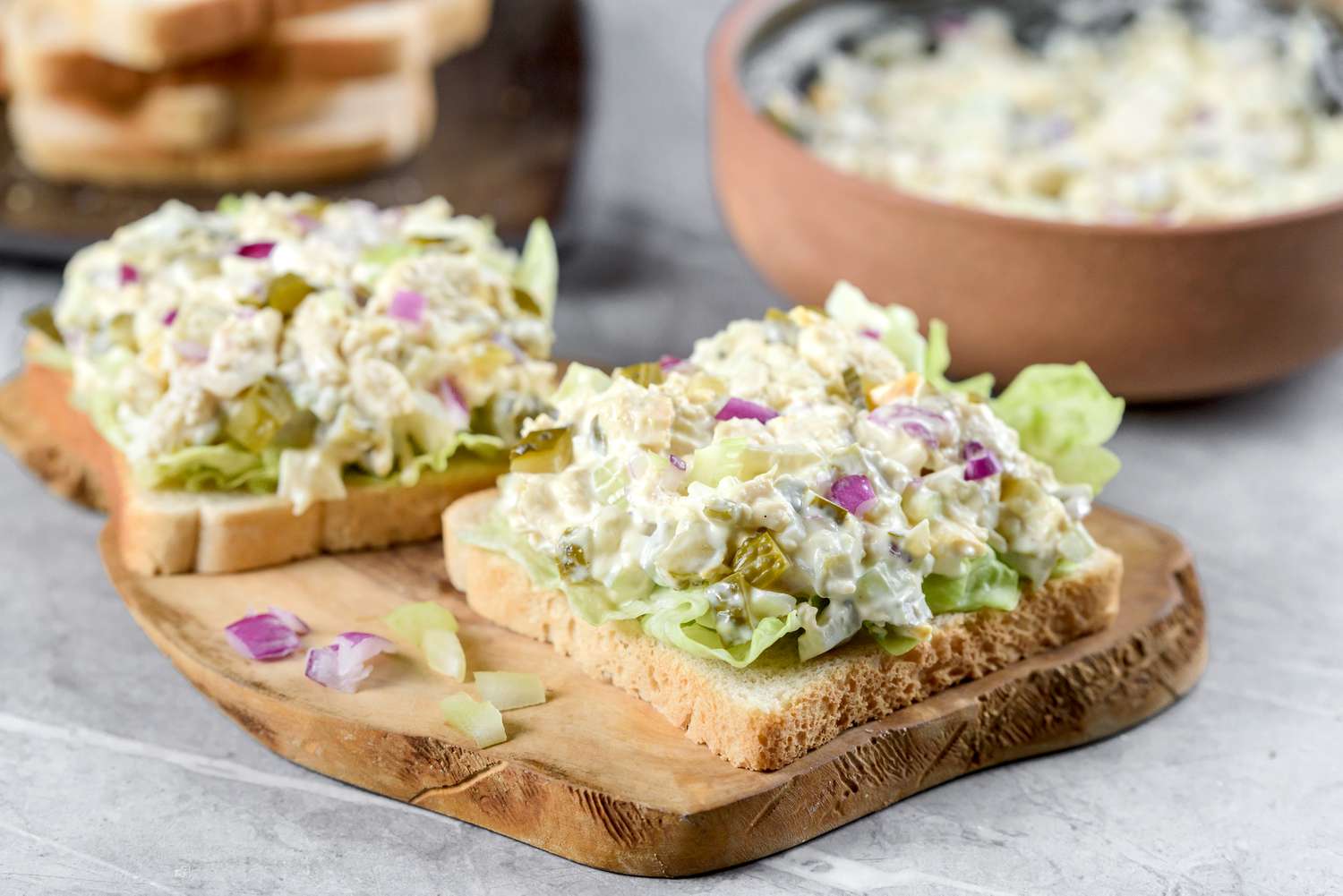 Two open face chicken salad sandwiches on a cutting board 