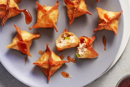 Several deep fried crab rangoons on a circular plate, one of them broken open so you can see the crab and cream cheese filling