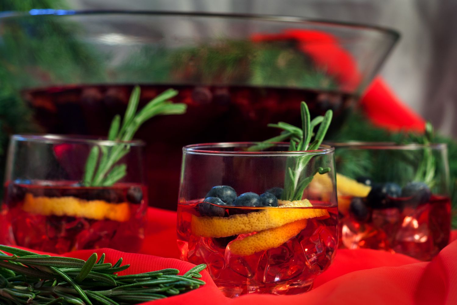 Glasses holing cranberry fresh gin punch garnished with rosemary, blueberries, and an orange peel