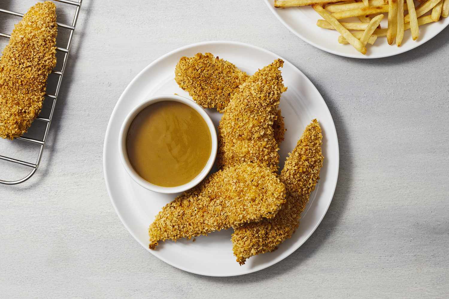 A plate holding four crispy baked chicken tenders and a ramekin of dipping sauce