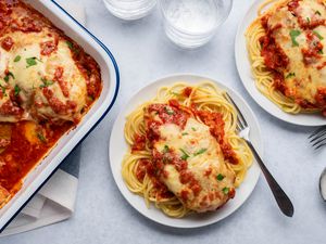 Chicken parmesan over pasta on a plate served from a casserole dish nearby