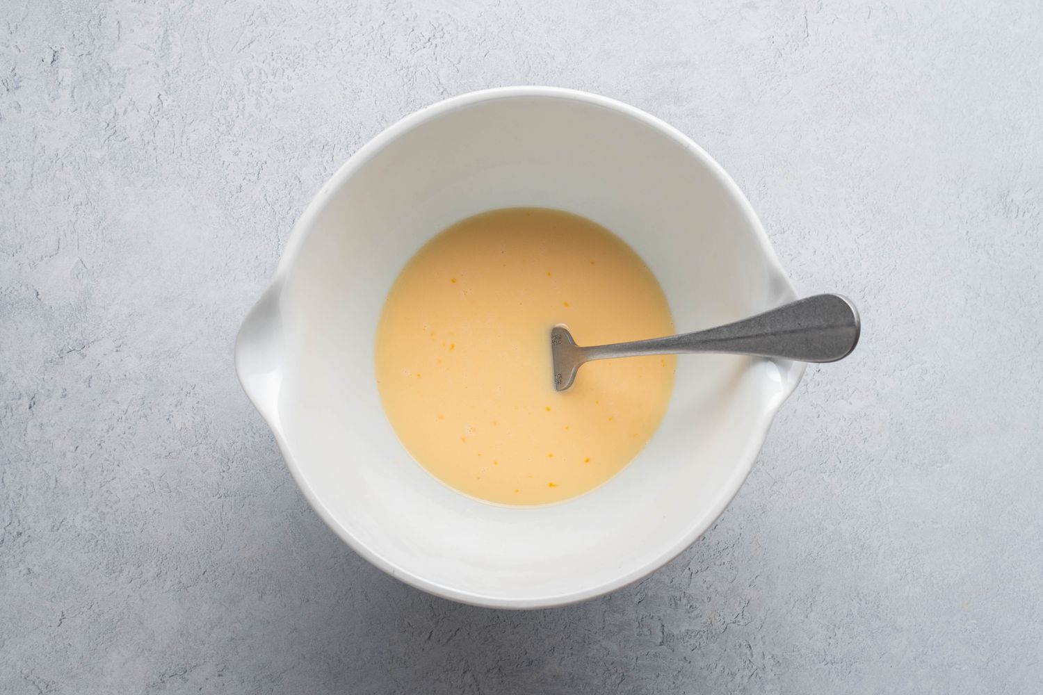 Egg and milk whisked together with a fork in a white bowl