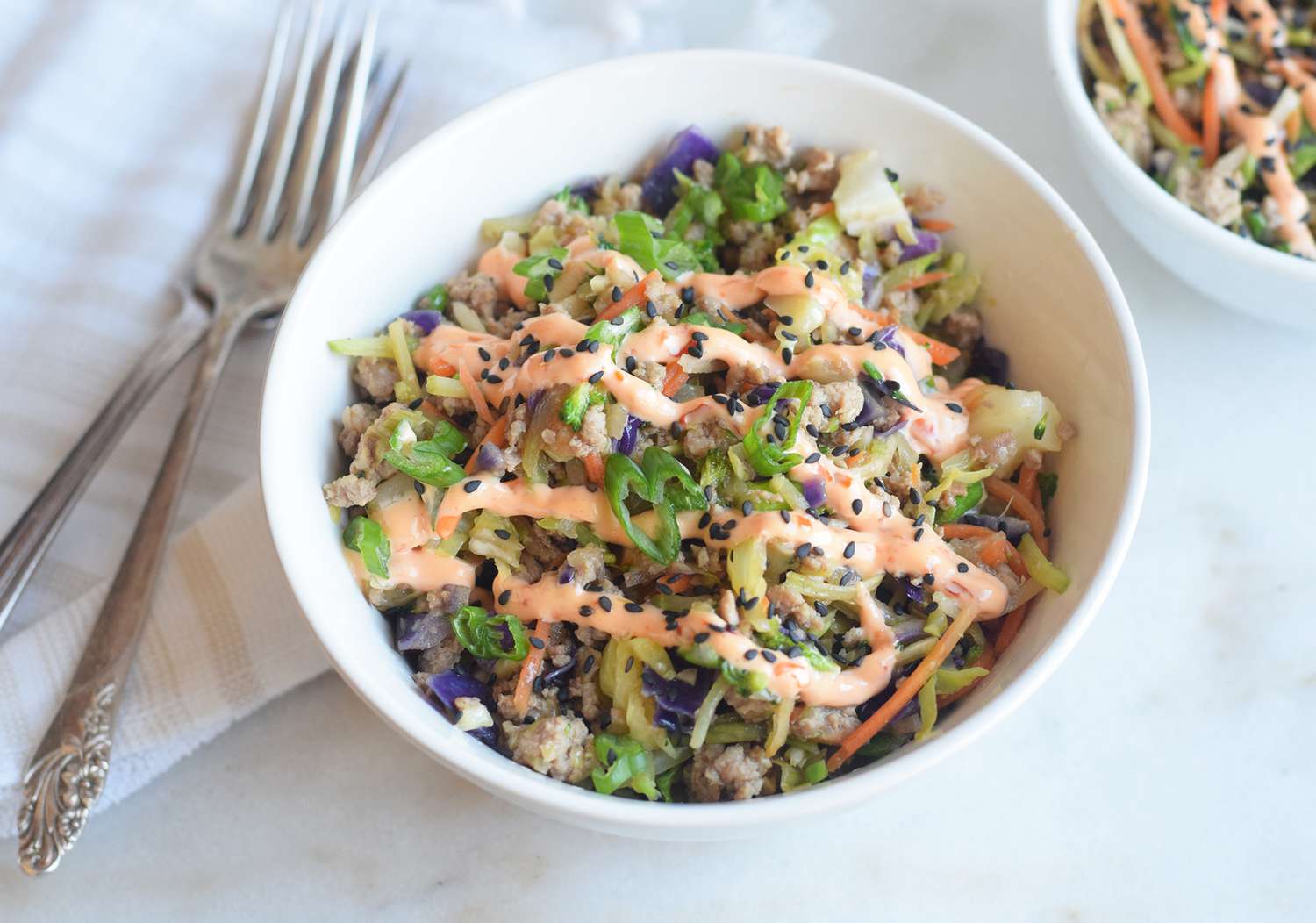 An egg roll in a bowl salad in a white bowl with two forks off to the side