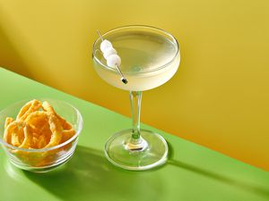 A Funyuns Gibson cocktail, served in a coupe, garnished with cocktail onions and served with a small bowl of funyuns