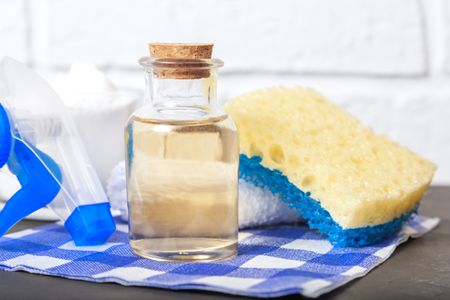 A bottle of apple cider vinegar surrounded by cleaning supplies. 