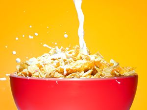 Milk flowing down into a red bowl filled with cereal