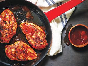 Three chicken breasts coated with barbecue sauce in a red skillet