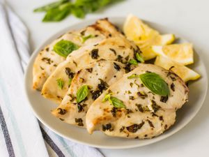 Lemon Basil chicken in a white bowl with lemons and basil as a garnish