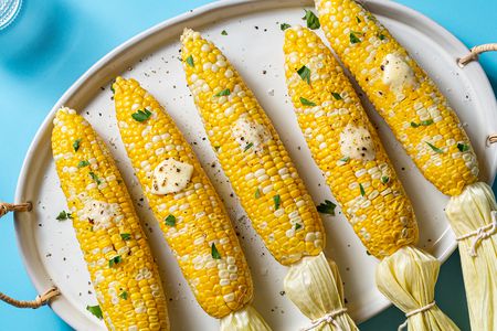 microwaved corn on the cobs on a serving platter with butter, parsley, and salt and pepper