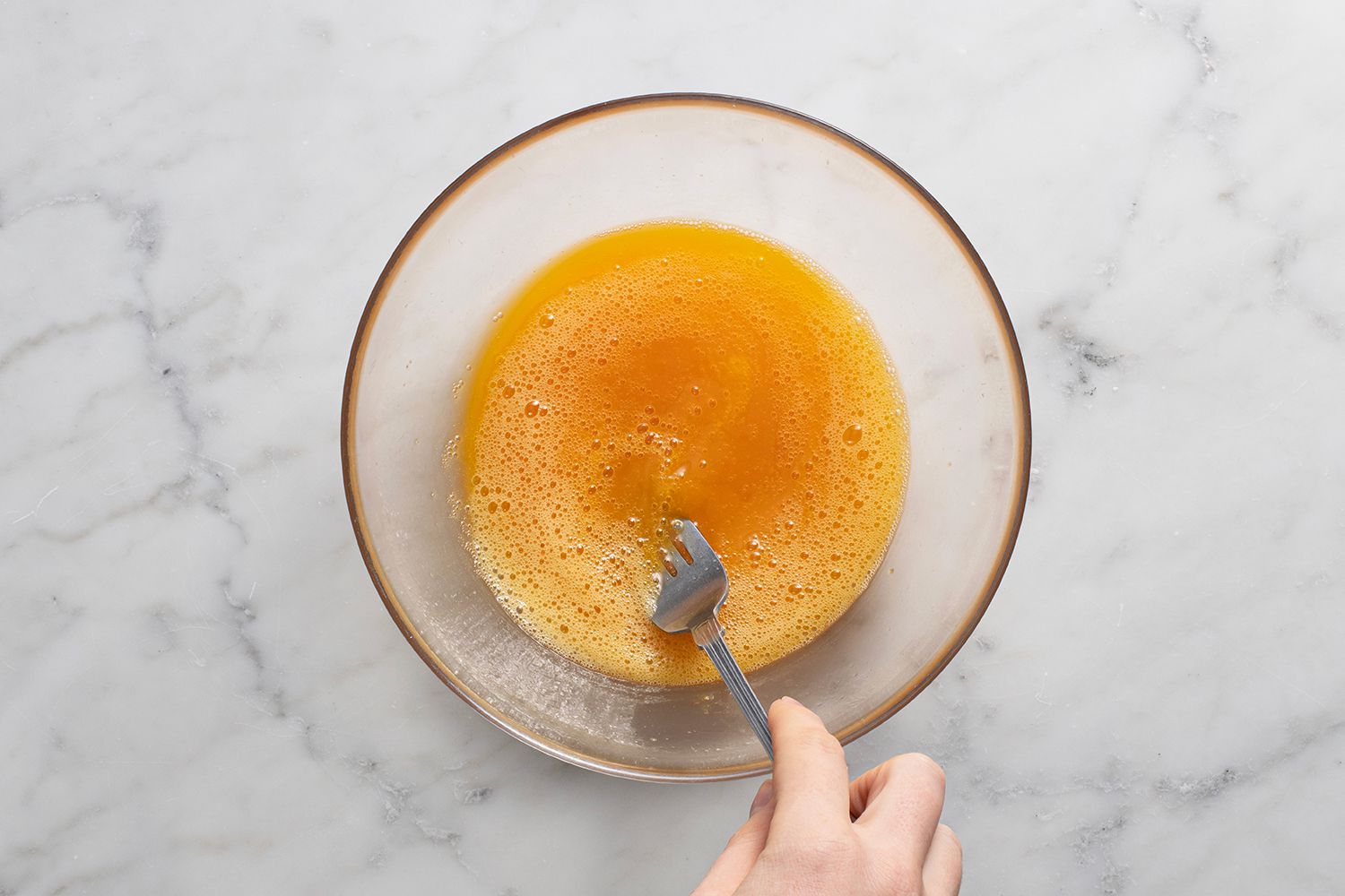 Eggs and salt in a glass bowl, stirred with a fork 