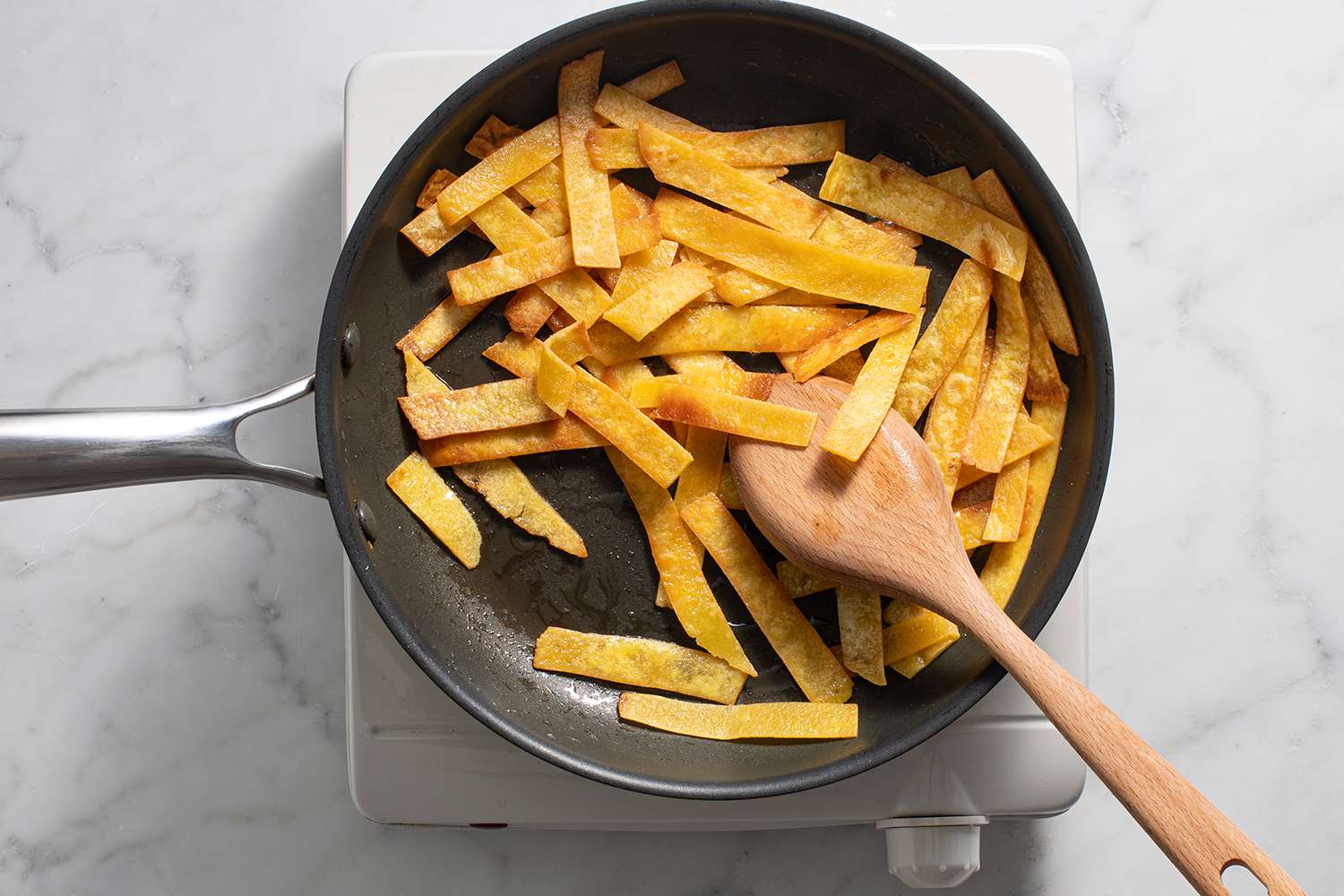 Tortilla slices in a pan with a wooden spoon, on a burner