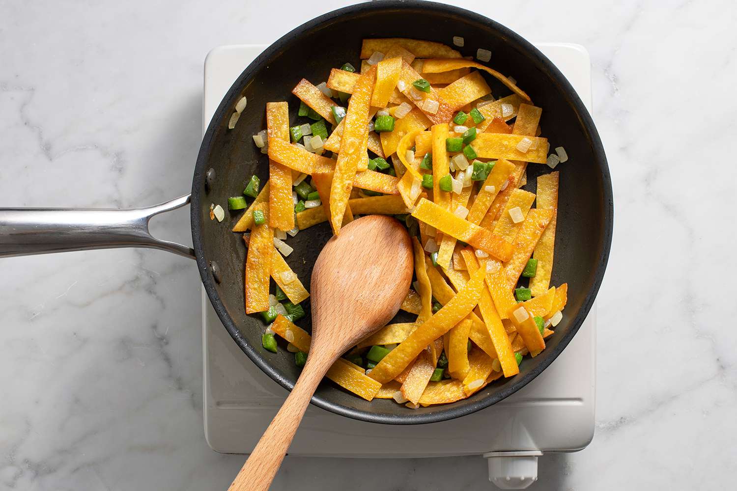 Tortilla strips, onions and peppers in a pan with a wooden spoon, on a burner