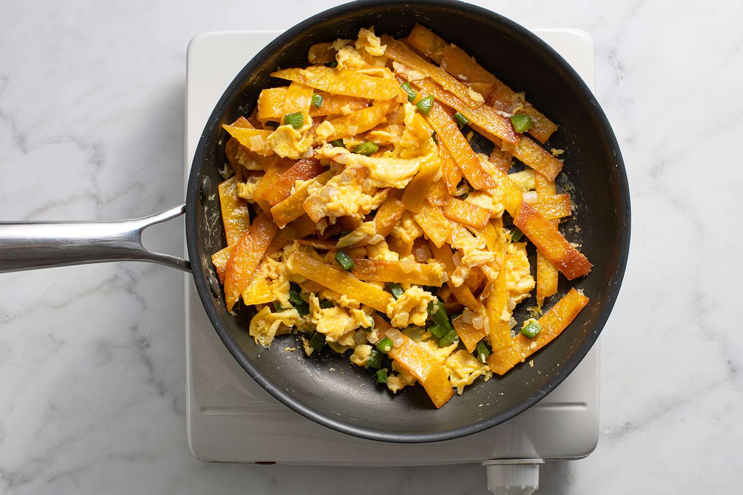 Eggs, tortilla strips, onions and peppers in a pan, on a burner 