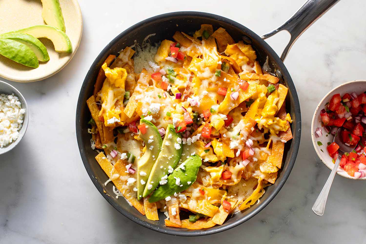 Migas in a pan, topped with avocado, cotija cheese, and salsa