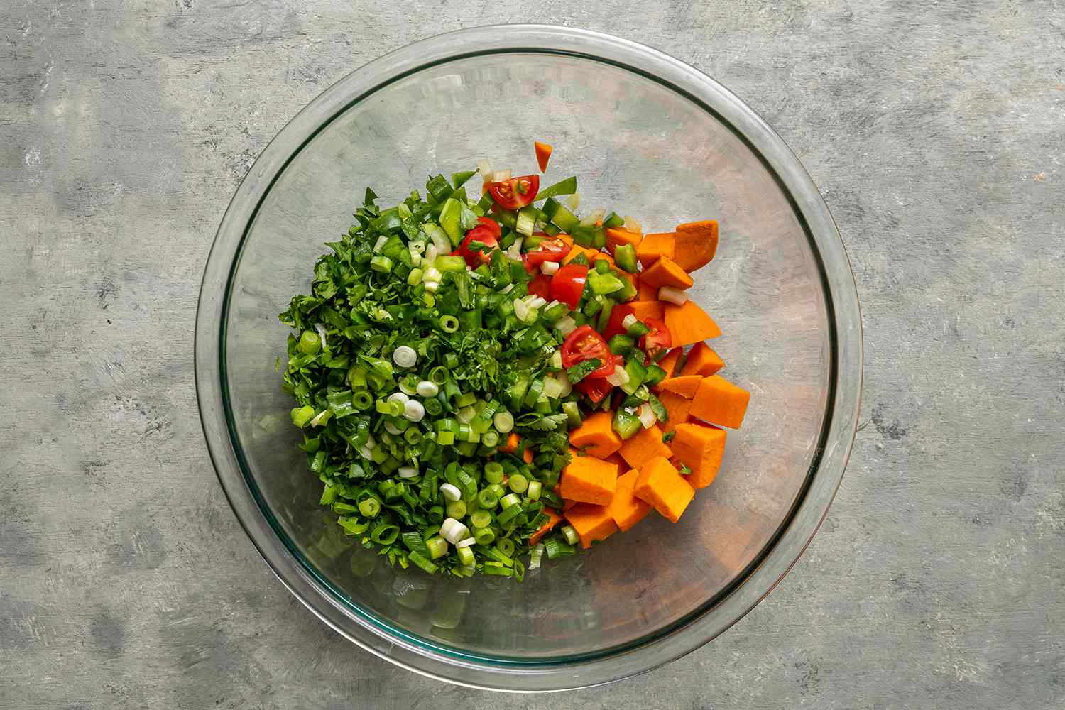 Green onions, sweet potatoes, bell pepper, celery, and cherry tomatoes in a glass bowl 