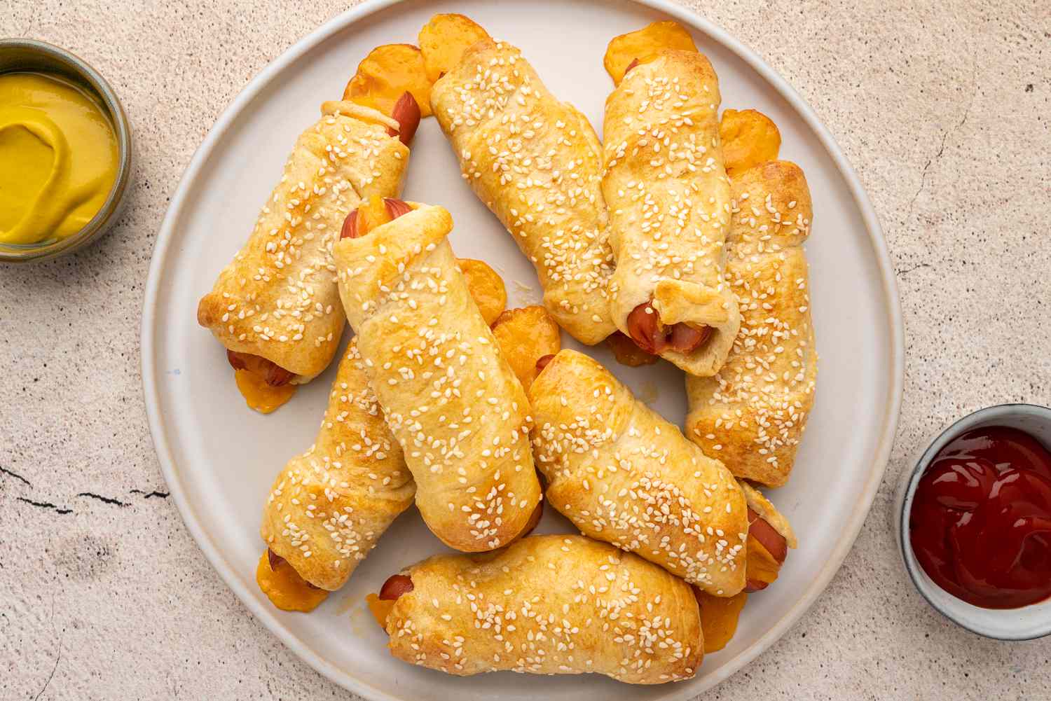 Crescent roll pigs in a blanket on a platter with ketchup and mustard in dishes off to the side