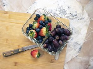 Prep Naturals Glass Meal Prep Container with strawberries, blueberries, and grapes displayed on a wooden cutting board