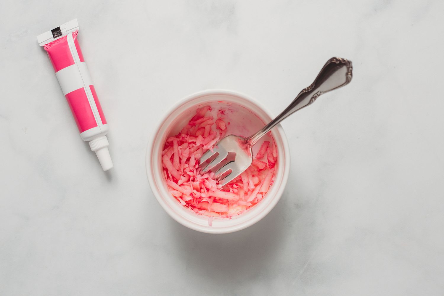 pink food coloring being mixed in one bowl of cheese with fork