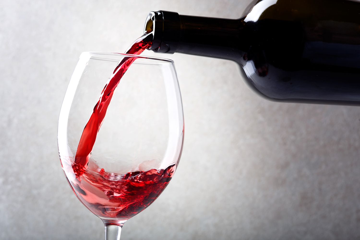 Red wine is poured into a glass from a bottle. Light background.