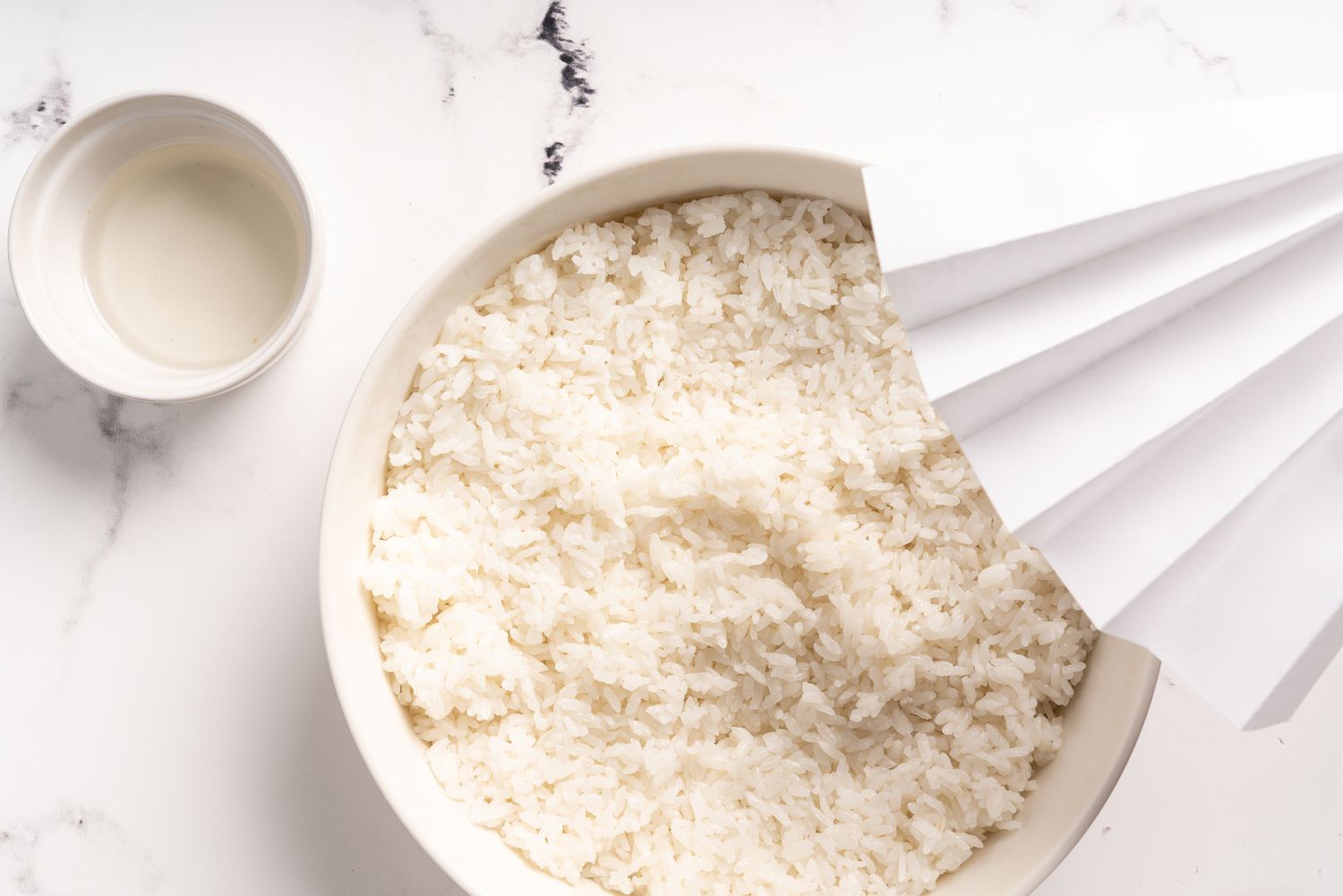 Rice in a bowl being cooled with a hand fan