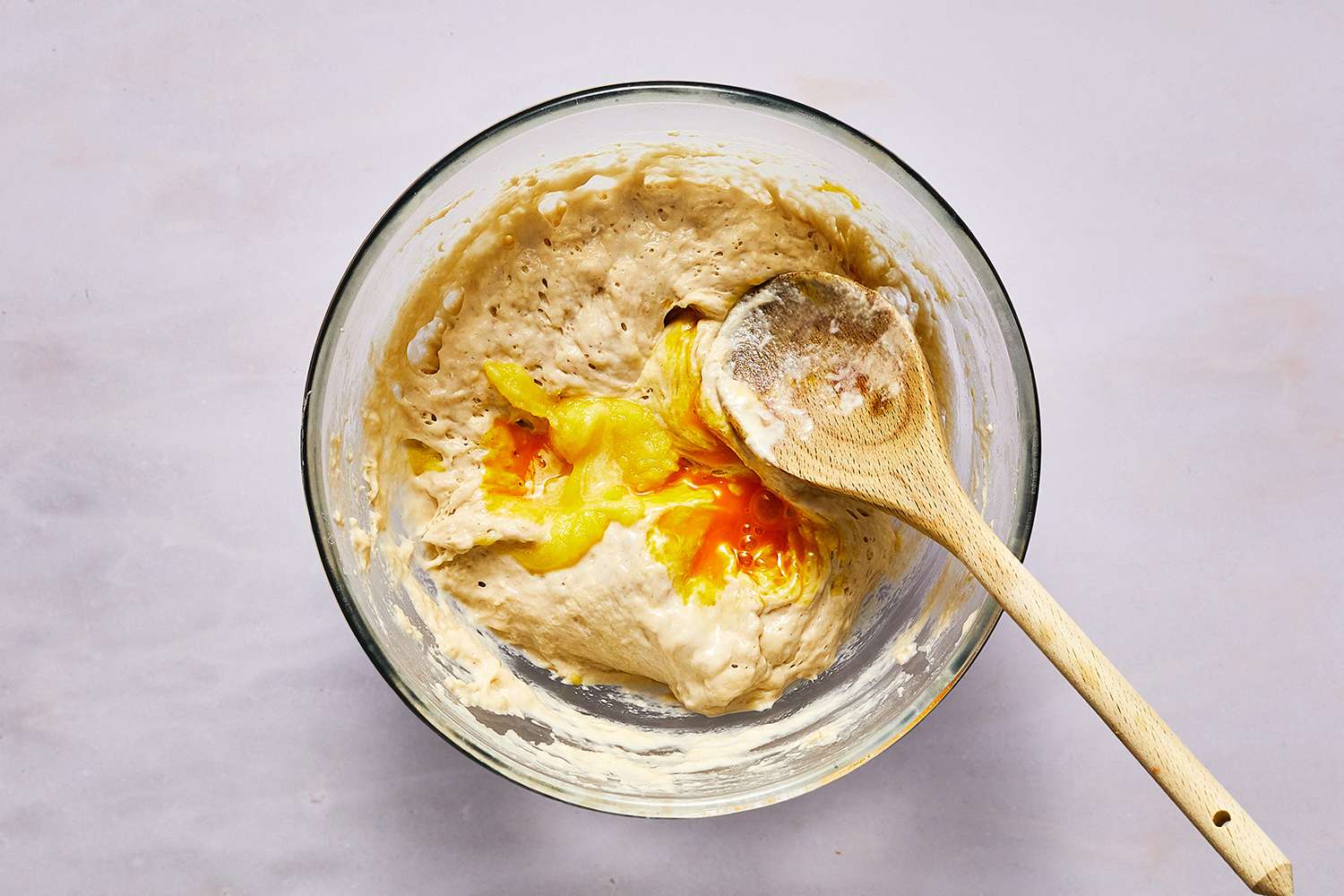 Blini batter in bowl with egg and a wooden spoon