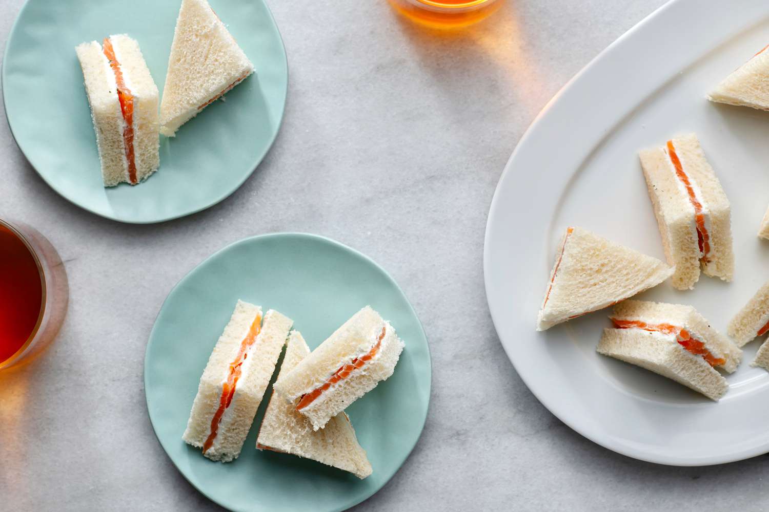 Two small blue plates and one large white platter with salmon and cream cheese tea sandwiches on them