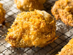 Fried chicken on a wire rack. There is one main piece in the center to the Fram and more pieces in the middle and background