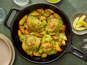 A skillet of roasted chicken thighs and parsnips, topped with an herb sauce, served with lemon wedges on the side