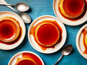 Five individual servings of mango flan with spoons on a blue surface