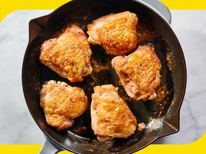 A cast iron skillet with five chicken thighs with crispy skin