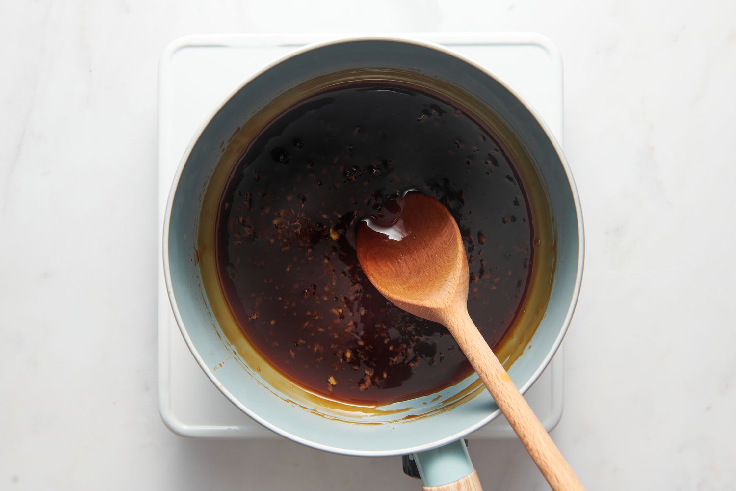 A small pan of honey-garlic sauce, with a wooden spoon mixing in cornstarch slurry