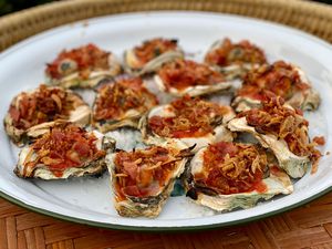 Delicious fresh oysters, topped with bacon, Worcestershire sauce, ketchup on a white ceramic plate.