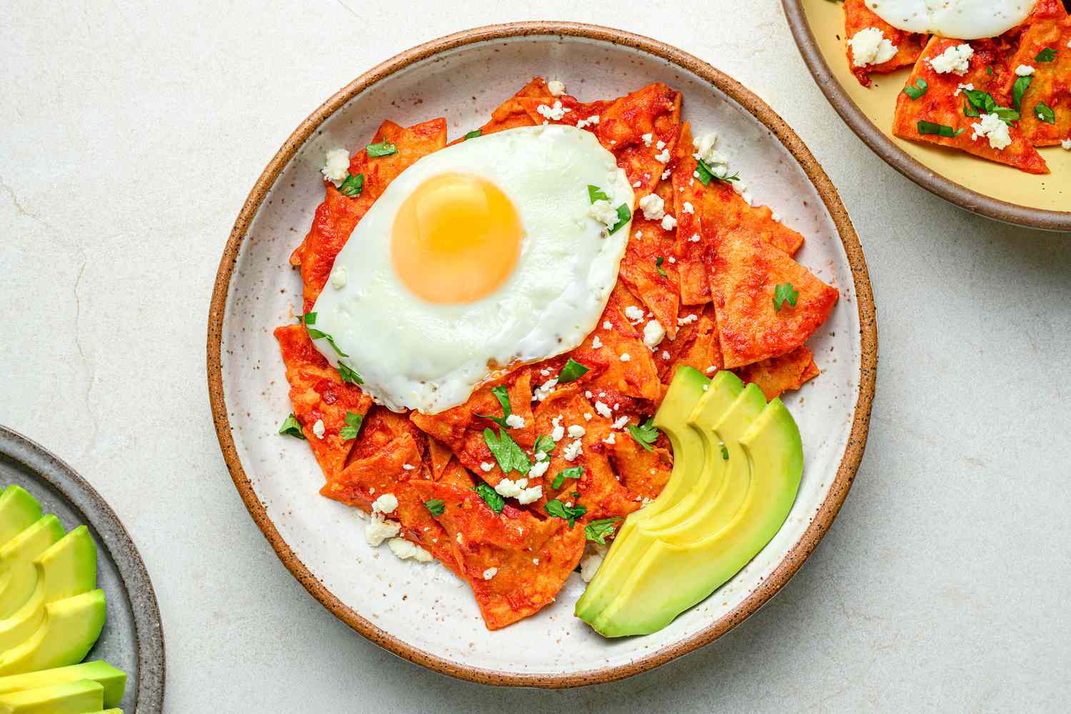 A serving of chilaquiles, stopped with a fried egg and served with sliced avocado