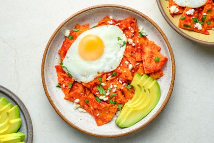 A serving of chilaquiles, stopped with a fried egg and served with sliced avocado