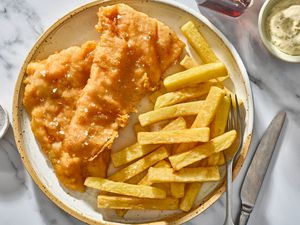 A plate of fried fish and french fries, served with malt vinegar and tartar sauce