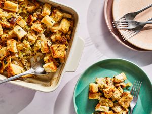 A casserole dish of baked stuffing, with a plated portion and extra plates and forks