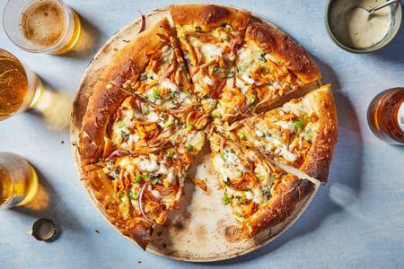 A buffalo chicken pizza cut into slices, served with glasses of beer