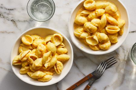 Two bowls of butternut squash macaroni and cheese with two glasses of sparkling water