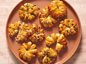 A large orange plate with caramel apple puff pastry doughnuts, garnished with pepitas, chocolate chips, and crushed pretzels