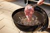 person flipping meat on a Weber Original Kettle Premium 22-Inch Charcoal Grill