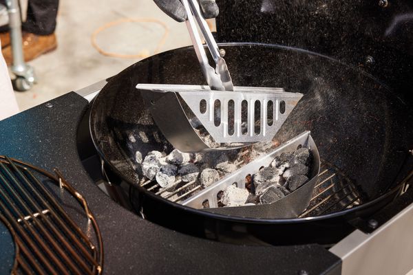 Hand with tongs placing grate above charcoals on the Weber Performer Deluxe