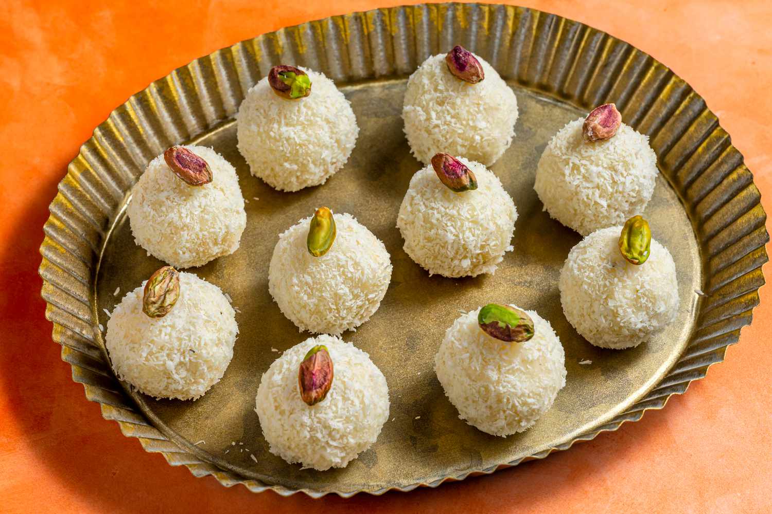 A fluted platter of coconut laddoo, topped with pistachios